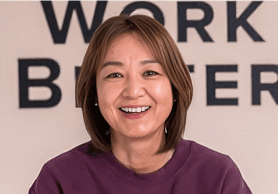 Smiling woman in purple top with blurred text background.